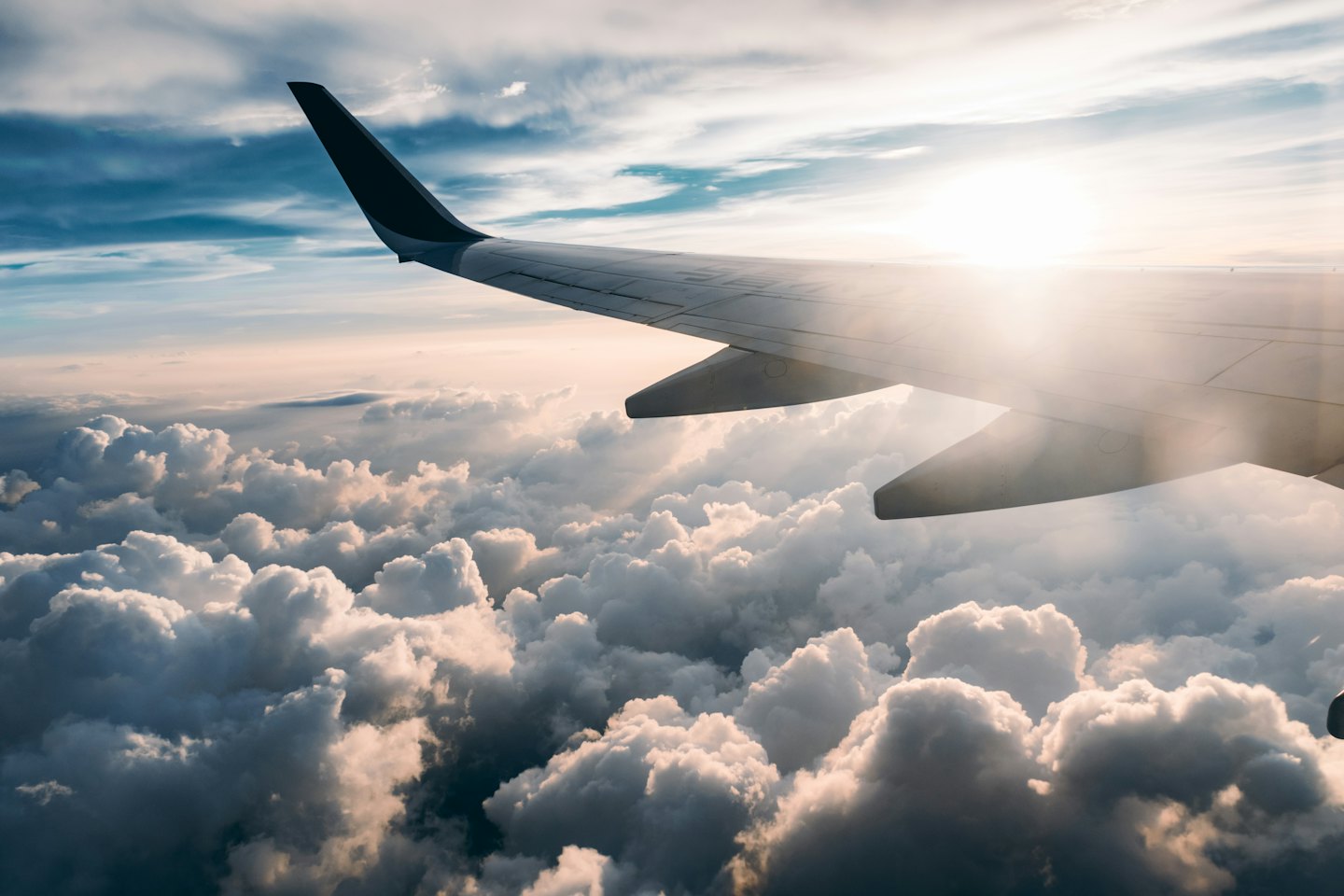 Airplane wing flying above clouds at sunrise.