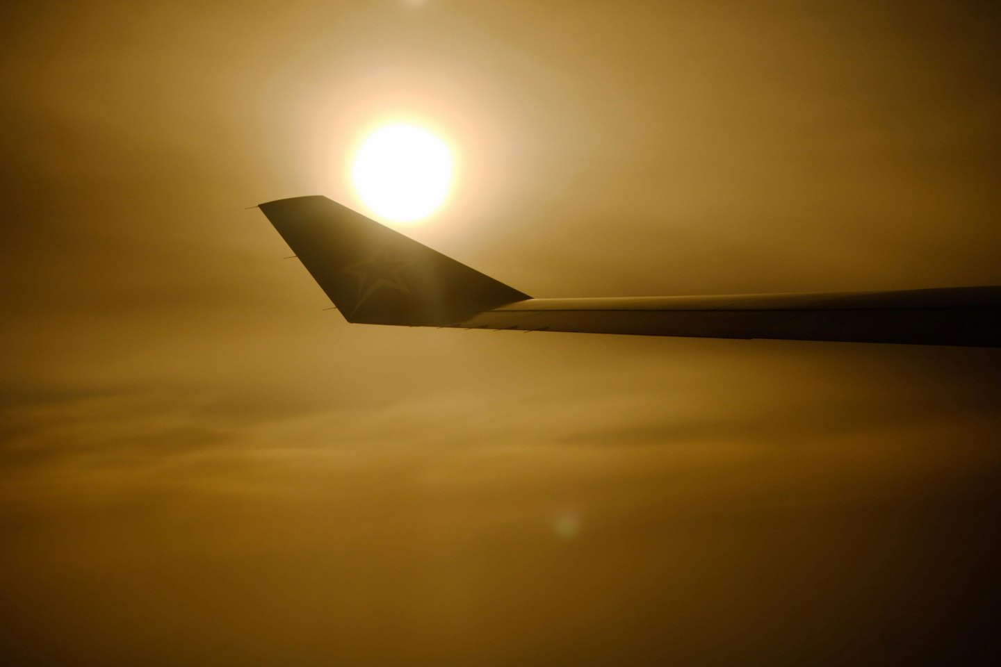 Airplane wing silhouetted against the sun above golden clouds.
