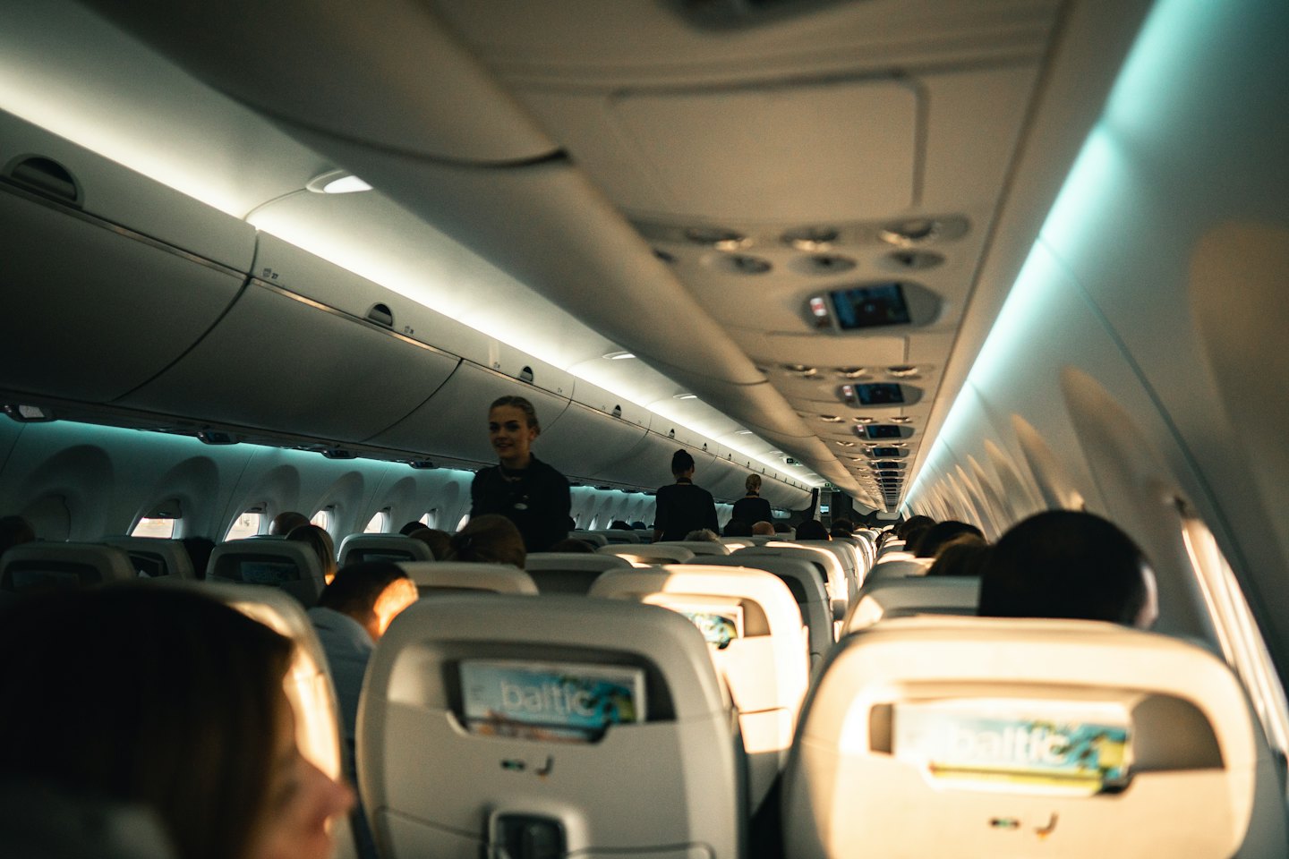 Flight attendant smiling while standing in a busy airplane aisle.