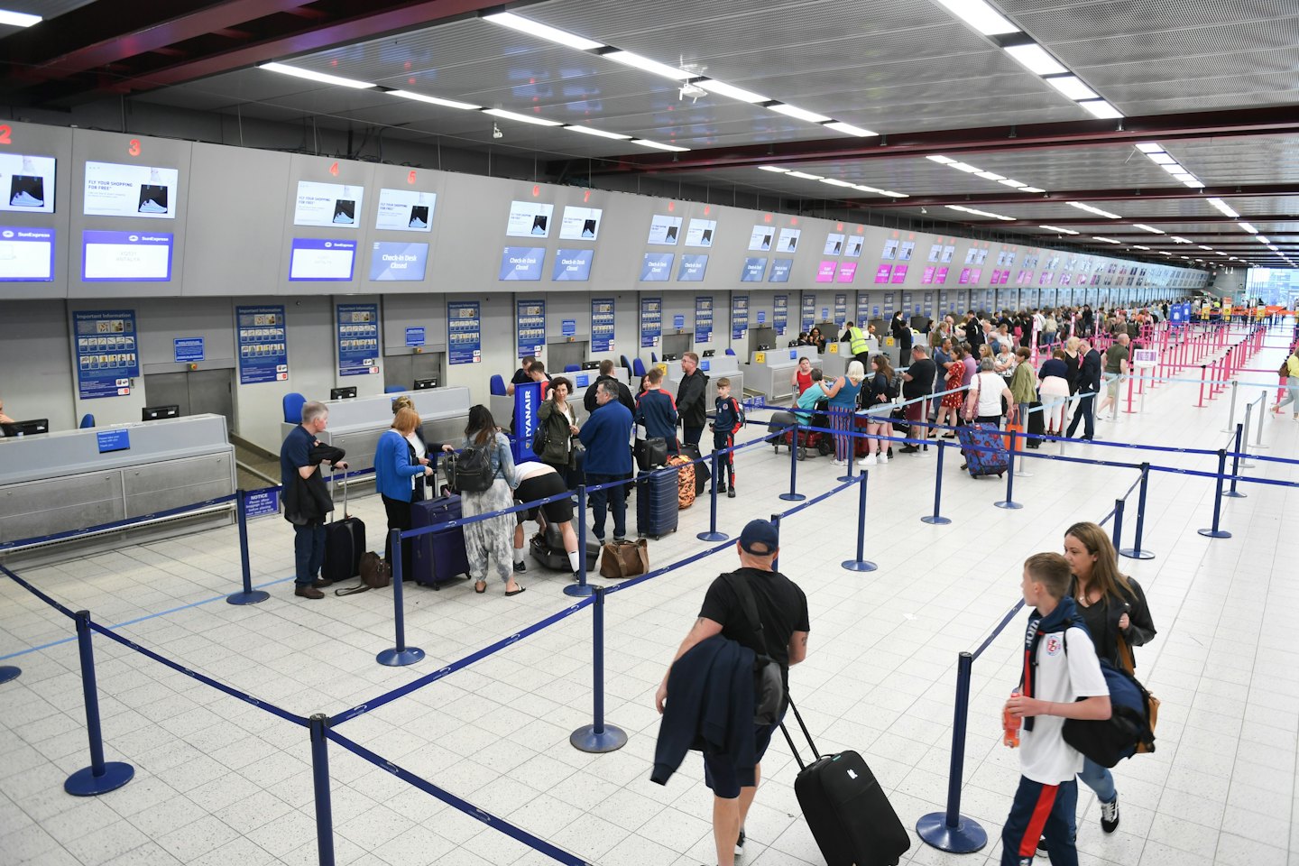 Travelers queue at modern airport check-in counters with digital flight information.