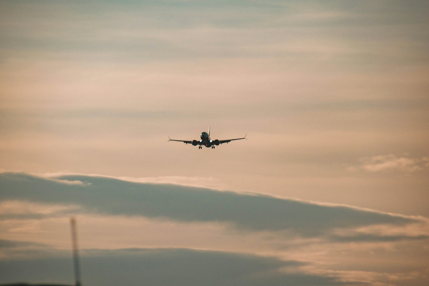 Commercial airplane landing with its gear extended against a cloudy sky.