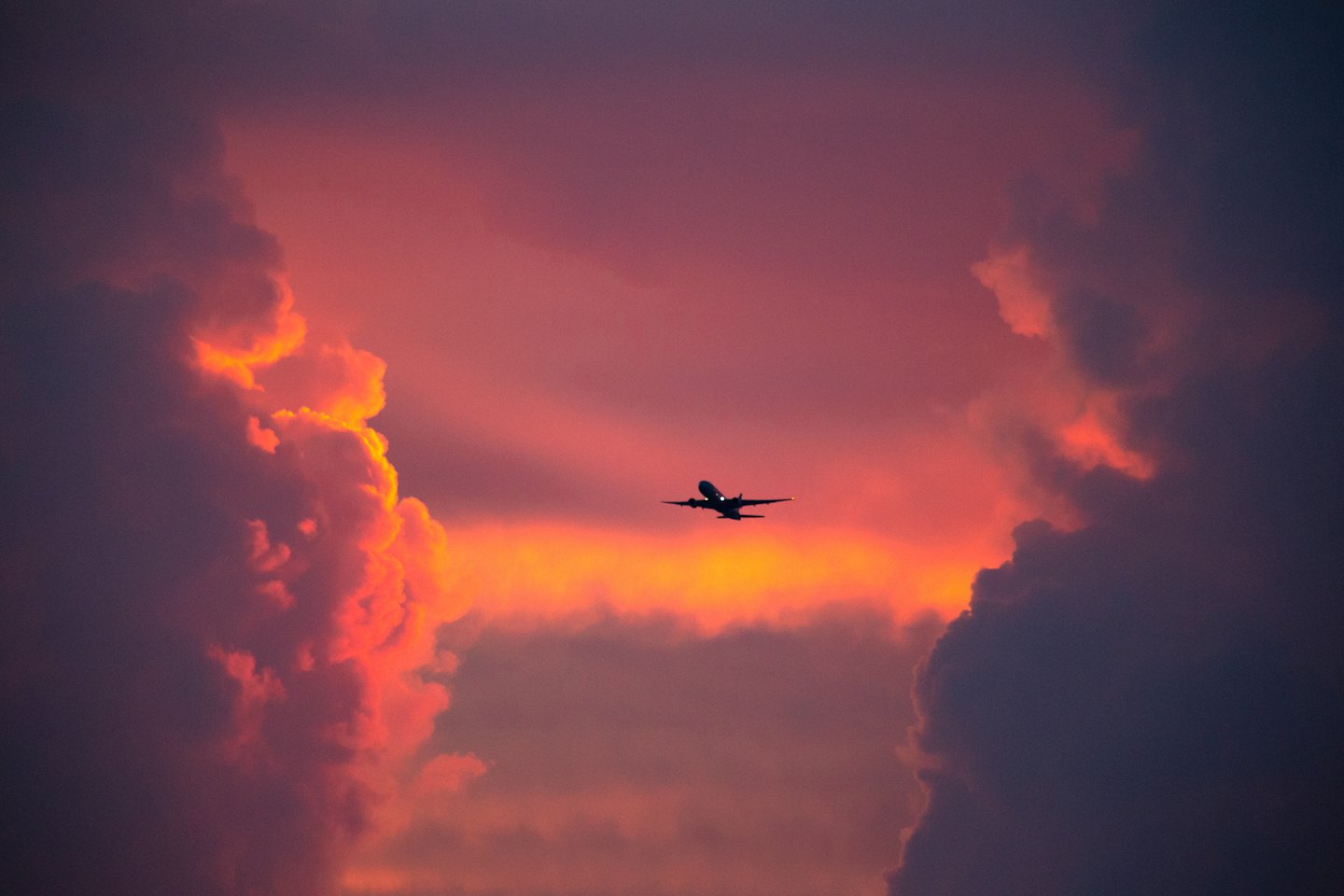 A commercial airplane flies through a colorful sunset sky.