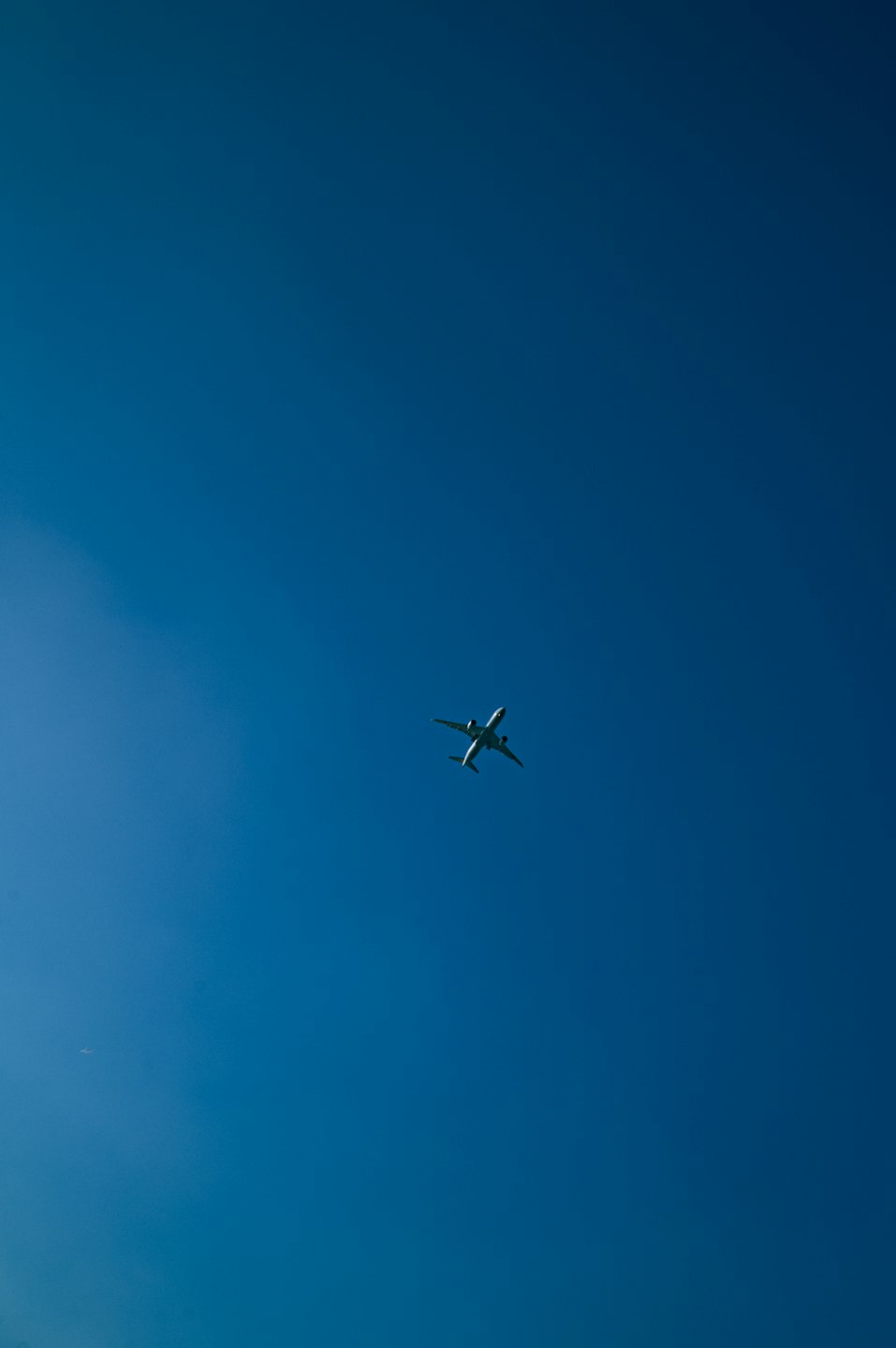 A white commercial airplane flies upward through a clear blue sky.