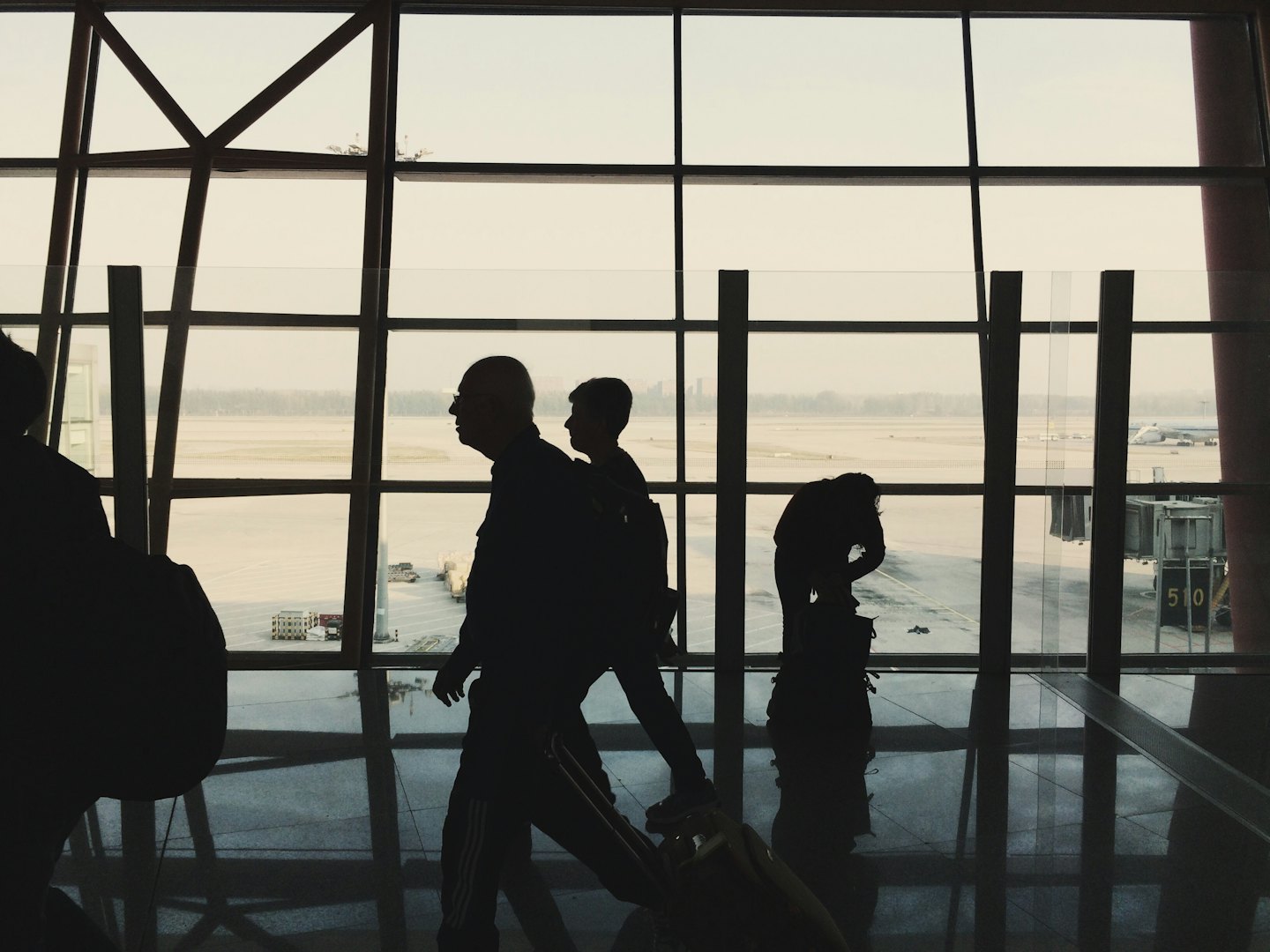 Travelers walk through an airport terminal past large windows.