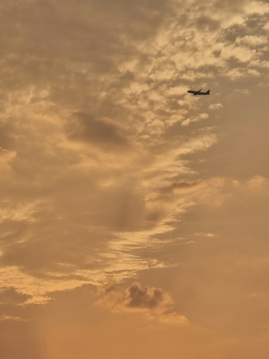 An airplane silhouette flies across a cloudy sunset sky.