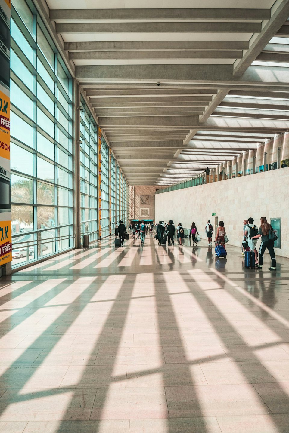 People walk through a modern airport with bright windows and stone walls.