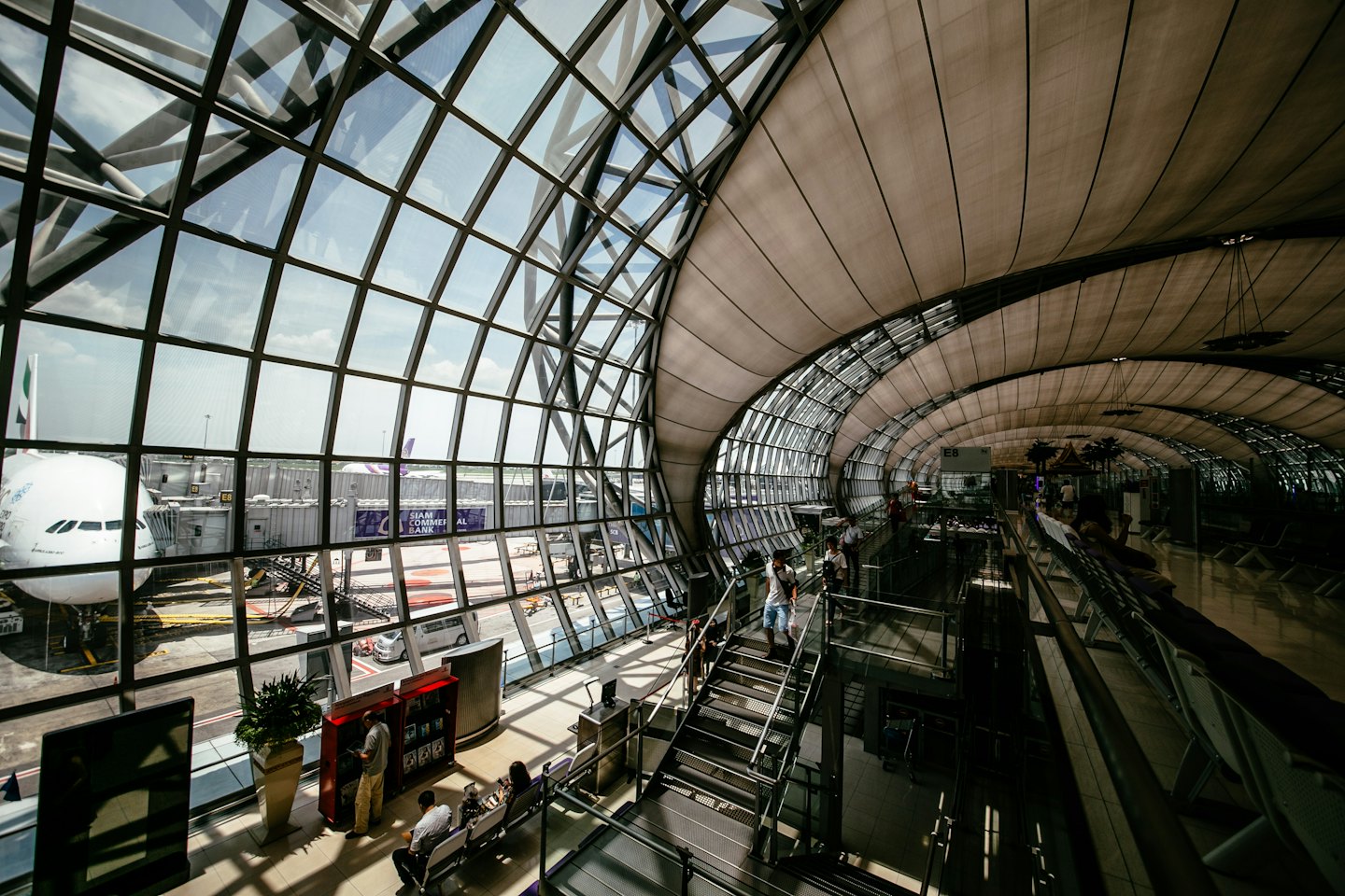 Modern airport terminal with passengers walking near large windows.